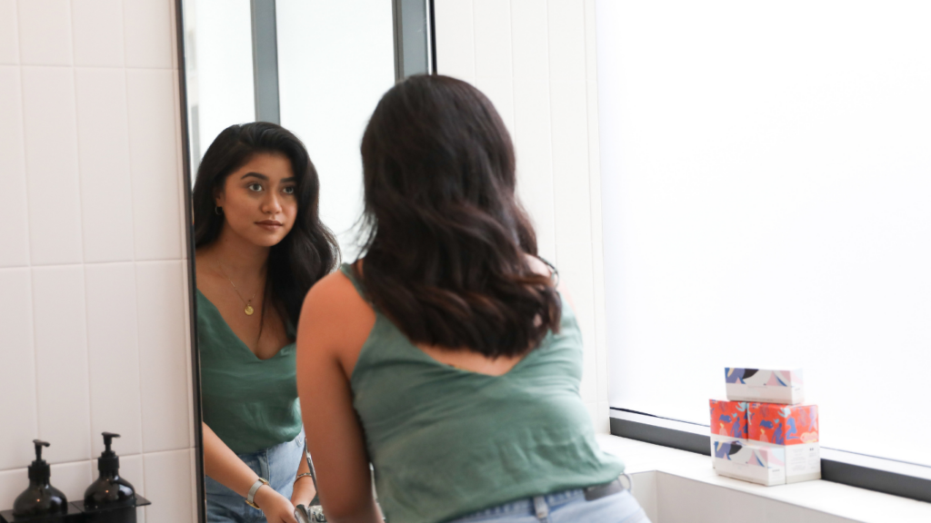a young woman looking in the mirror being self-aware.